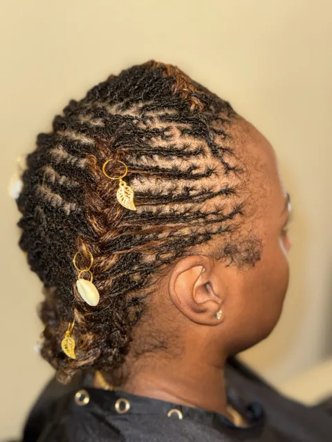 Side view of locs swept into a sculpted style with gold and shell accents at September’s Locs
